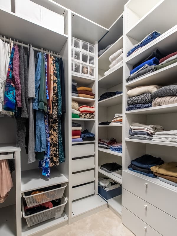 Białe szafy PAX i PLATSA w małej garderobie z ubraniami.