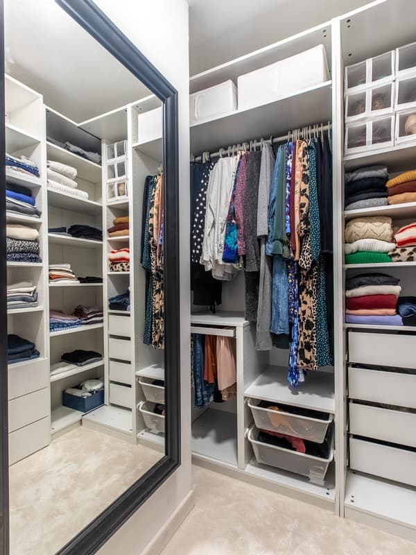 Białe szafy PAX i PLATSA w małej garderobie z ubraniami.