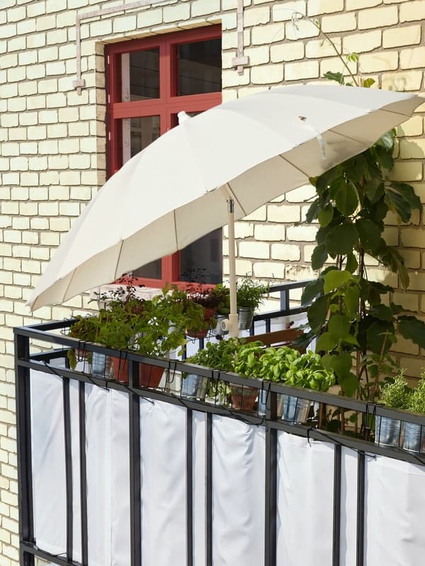 Biały parasol SAMSÖ/GRYTÖ odchylony tak, by chronił przed słońcem i zapewniał cień.