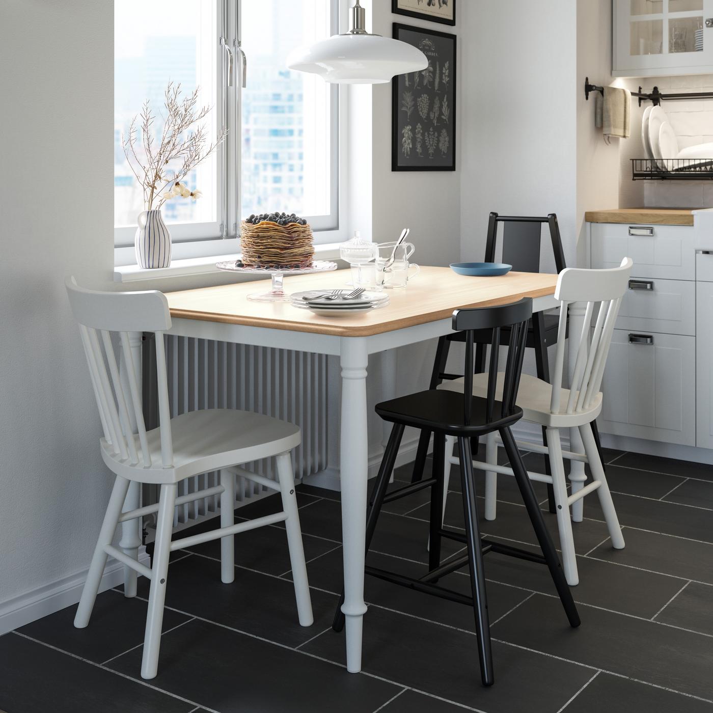 Biały stół i 4 krzesła stoją w niewielkiej kuchni.