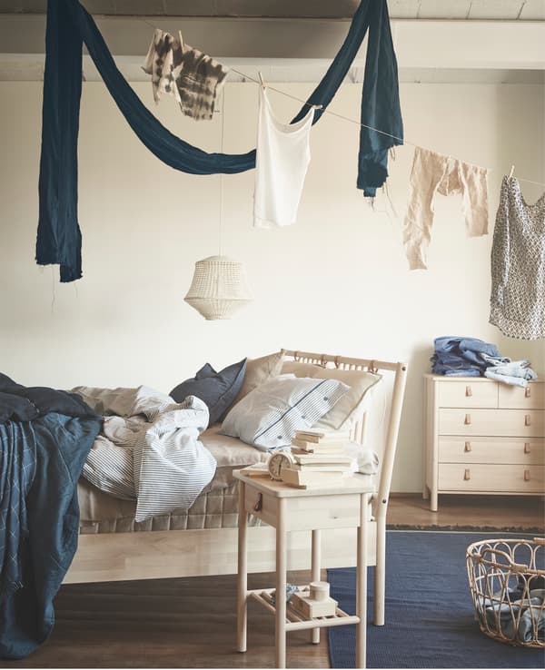 Biancheria appesa sopra a una struttura letto BJÖRKSNÄS, un comodino e una cassettiera in legno.