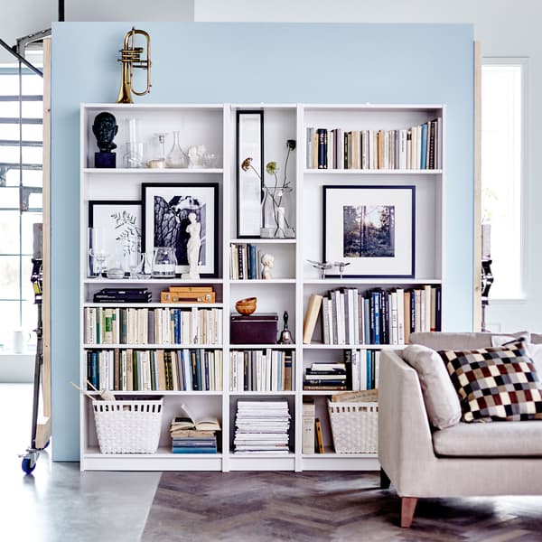Bibliothèques BILLY blanches remplies de livres, photos et objets personnels. Dans le bas, des paniers de rangement.