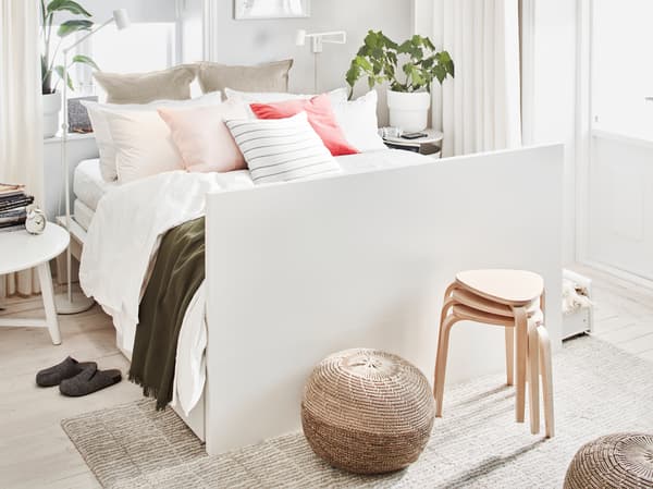 Biela dvojmiestna posteľ MALM s množstvom vankúšov a čelom postele umiestneným na konci uprostred svetlej miestnosti.