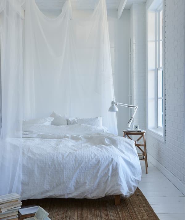  Biela spálňa s bielymi posteľnými obliečkami a priehľadnými bielymi závesmi okolo postele. 