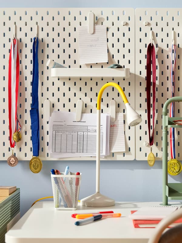 Bielo-žltá pracovná LED lampa NÄVLINGE na stole RELATERA pred nástenkou SKÅDIS.