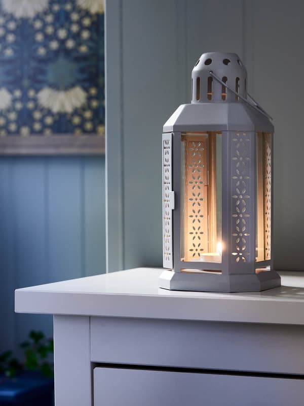 Biely lampáš ENRUM stojí na bielej komode.