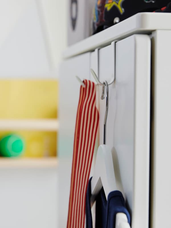 Biely vešiak BUMERANG visí na dverách skrine na bielom háčiku LÄTTHET.