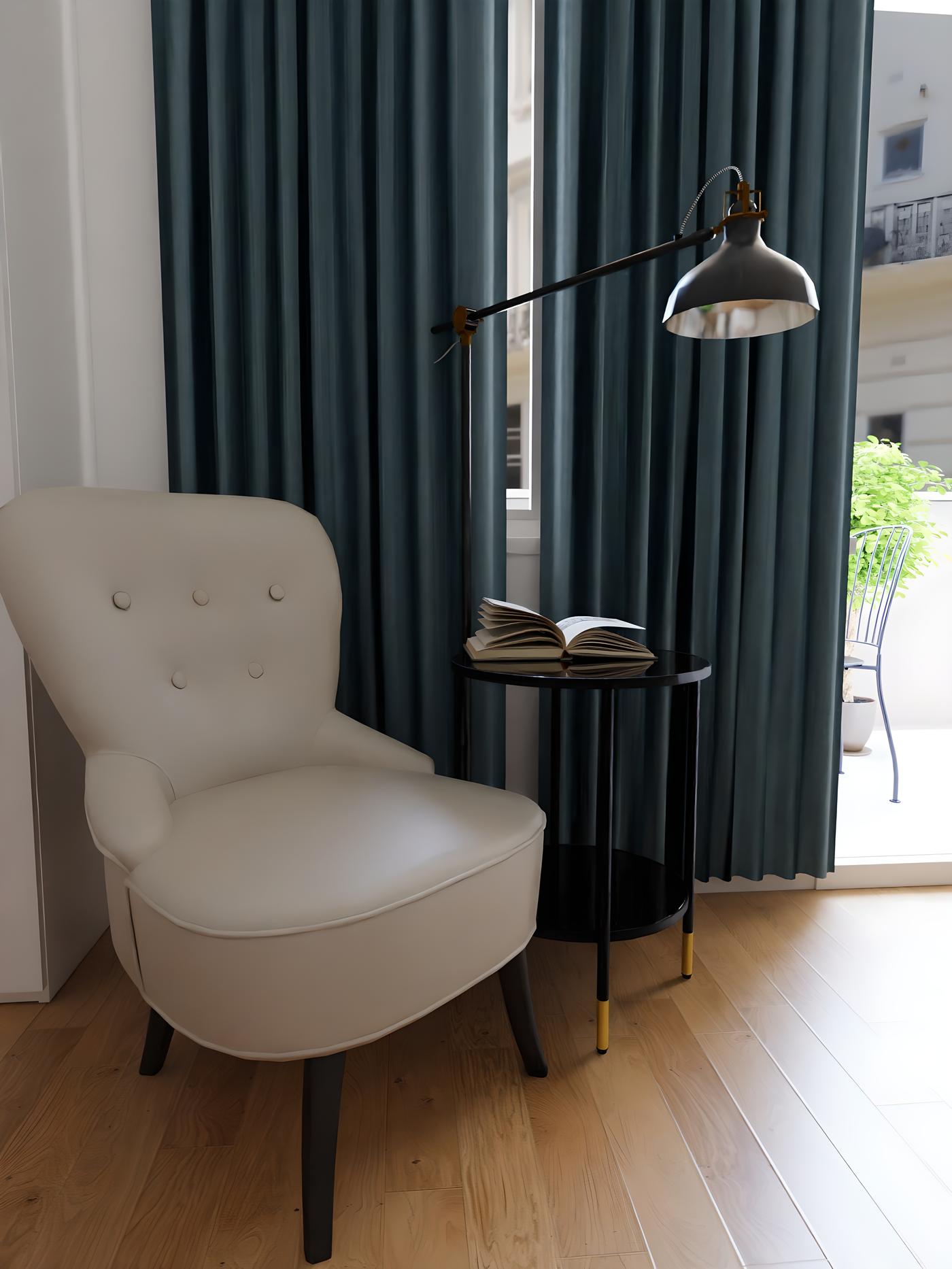 Bijela fotelja, crni stolić s otvorenom knjigom i metalna lampa ispred plavih zavjesa u svijetloj sobi.