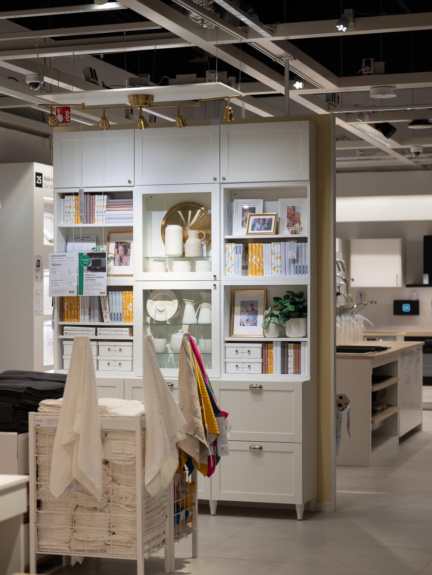 Bijela polica s knjigama, ukrasima i biljkama u modernom interijeru trgovine namještajem.