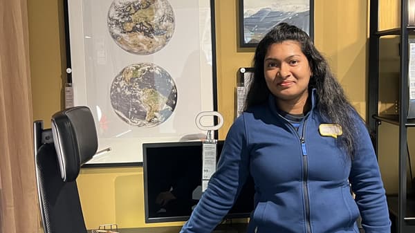 Bild på Gayathri Ramajeyam. Hon har en blå kofta på sig, svart hår och bruna ögon. Hon står framför ett skrivbord med en datorskärm.