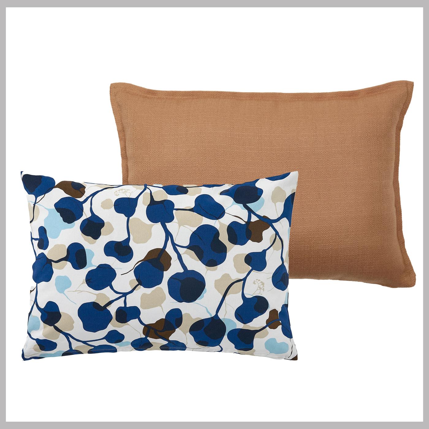 Bild på två rektangulära frilagda prydnadskuddar mot vit bakgrund. Den ena är vit med blått och brunt bladmönster och den andra är enfärgad brun. 