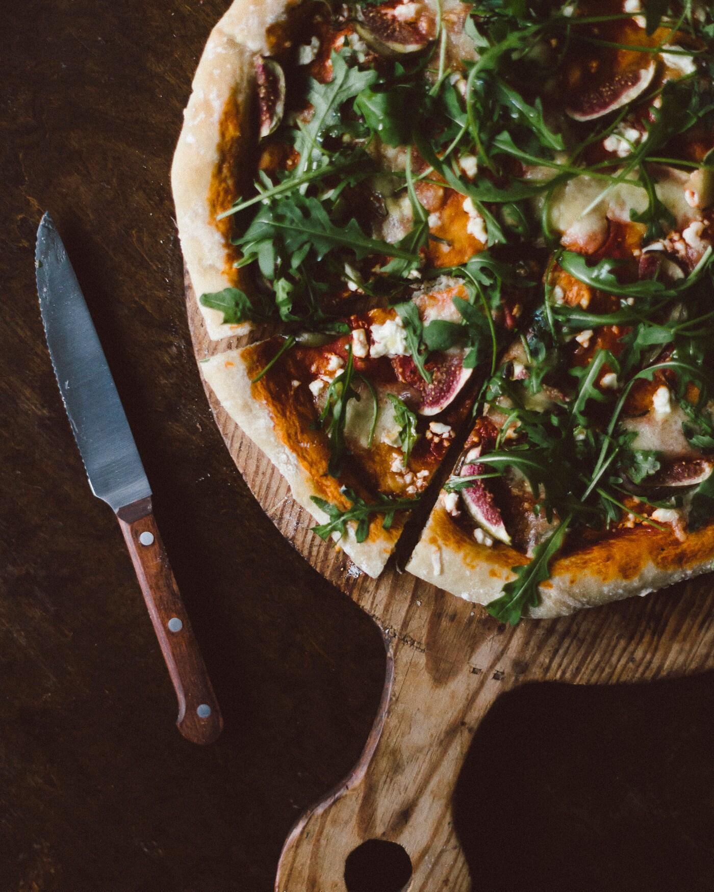 Bild tagen uppifrån på en pizza med getost, fikon och ruccula.