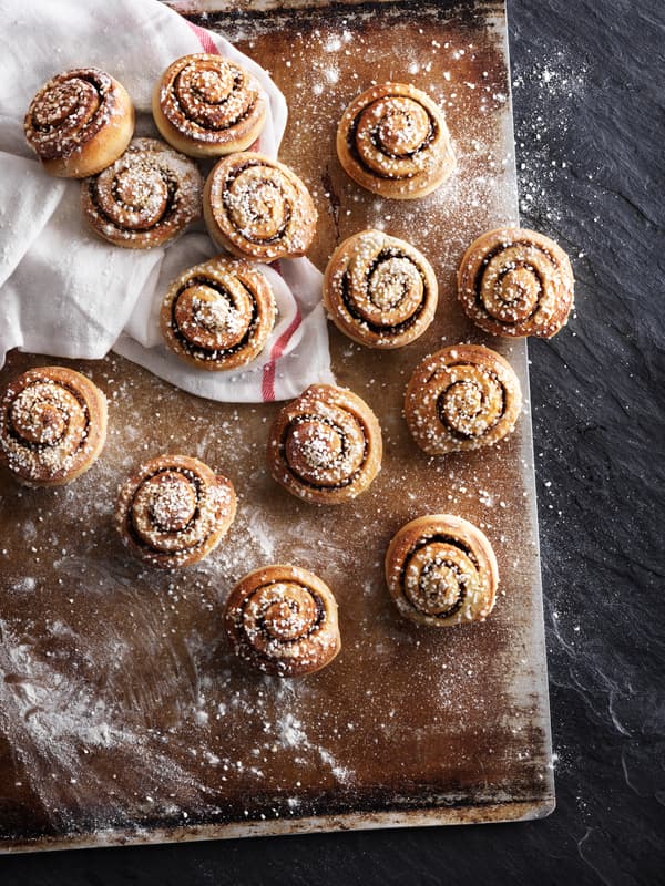 Bild tagen uppifrån på nybakade kanelbullar på en plåt.