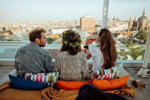 Bild zeigt 3 Personen die auf einer Betonbank den Ausblick über Wien genießen.