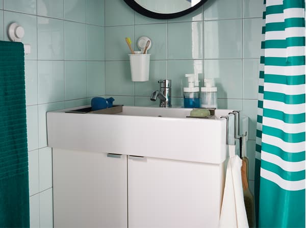 Bilik mandi berwarna hijau dengan gambar dekat kabinet sink cuci tangan berwarna putih yang dikelilingi dengan tuala, sabun dan berus gigi.