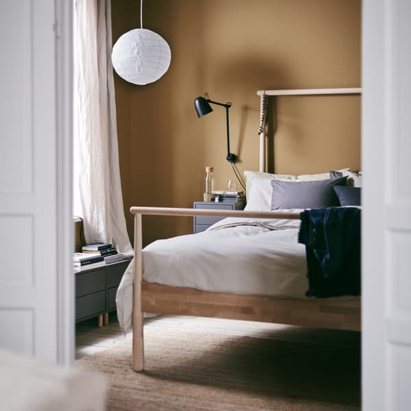 Bilik tidur dengan rangka katil GJÖRA diperbuat daripada kayu birch dengan sarung duvet ÄNGSLILJA berwarna kelabu-kuning air dan lampu pendan REGOLIT buatan tangan di atas.