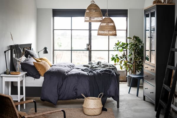 Bilik tidur yang mempunyai katil HEMNES berwarna gelap terletak di tengah-tengah, tingkap Perancis di sepanjang satu dinding dan perincian yang dibuat daripada bahan semula jadi dengan warna semula jadi.