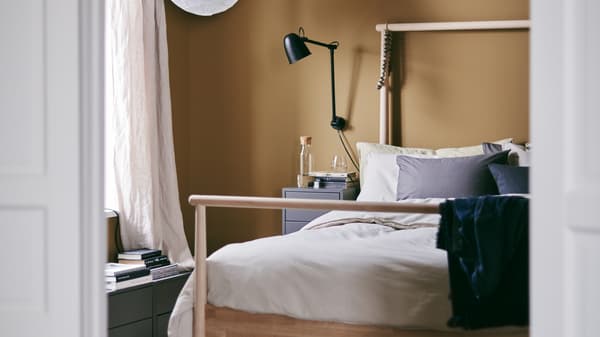 Bilik tidur yang nyaman dan selesa dengan dinding berwarna karamel pekat dan rangka katil GJÖRA yang dibuat daripada kayu birch padu dan meja sisi katil.