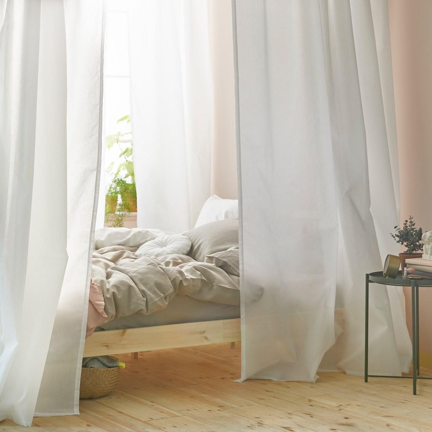 Bilik tidur yang terang yang mempunyai katil dekat dengan tingkap. Katil itu mempunyai kanopi yang dibuat menggunakan langsir berwarna putih yang tergantung pada trek langsir VIDGA.