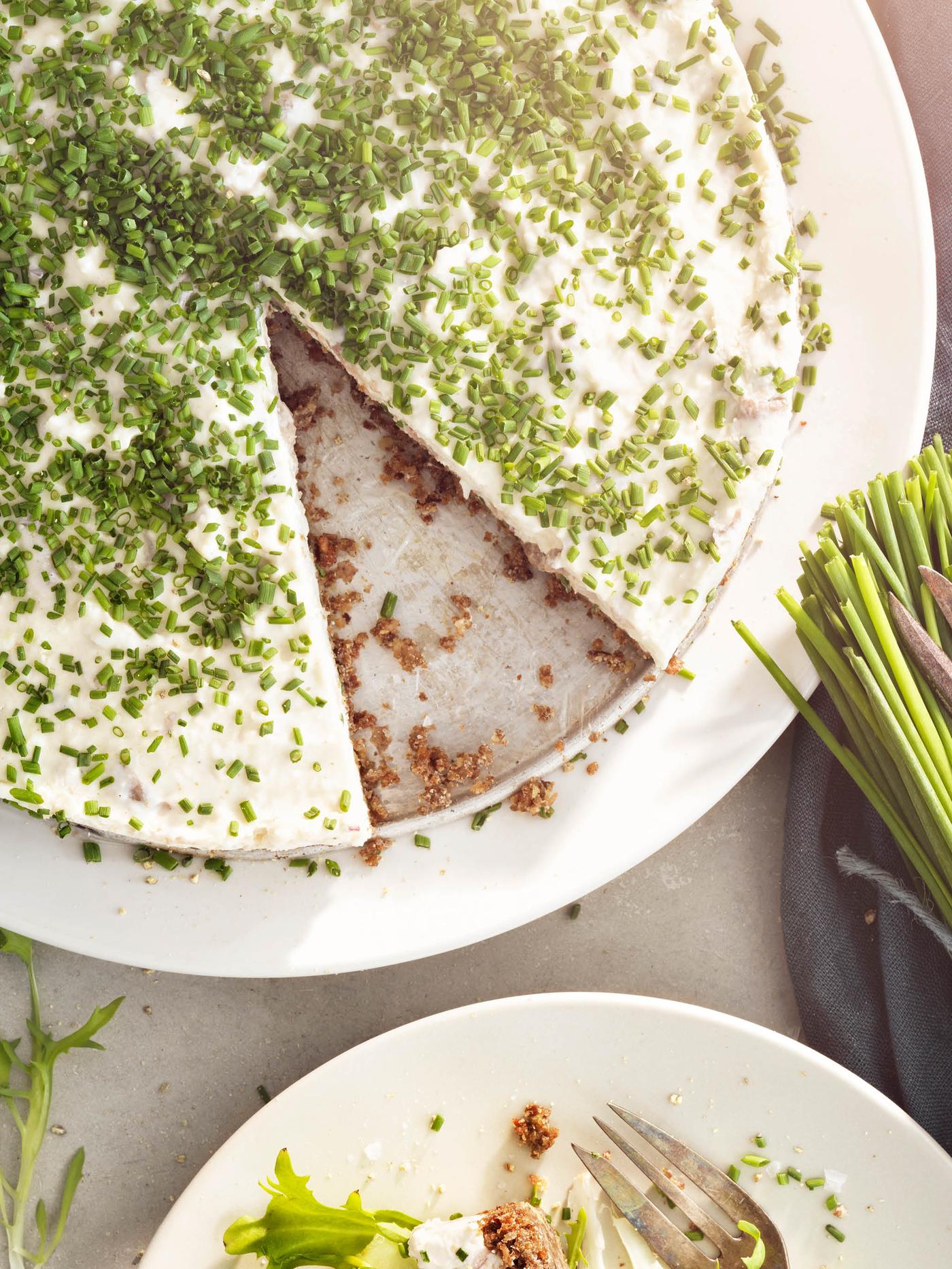 Bílý talíř se sleďovým dortem ozdobeným pažitkou, vedle leží svazek pažitky.