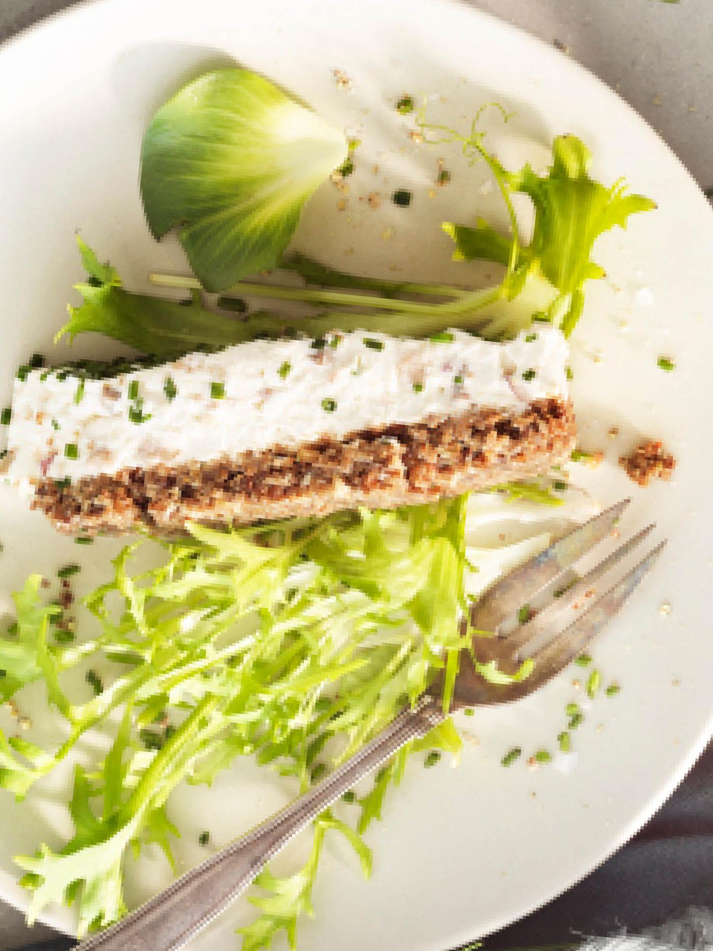 Bílý talířek s dílkem sleďového dortu ozdobeného lístky salátu.