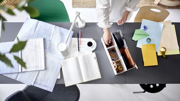 bird view of a desk with documents and planning tools, and a person reaching their hand to grab something from the tool organizing box 