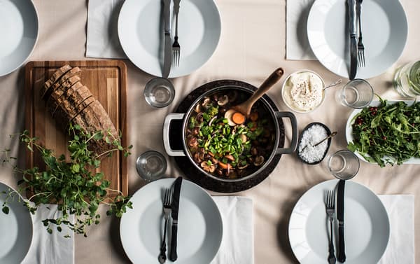 Bird’s-eye view of a pot of food on a table with plate settings.