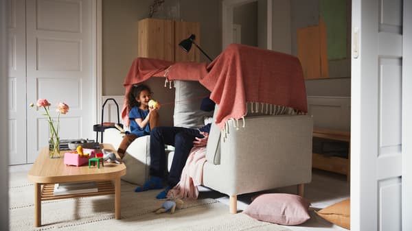 ベージュのPÄRUP/ペルプ ソファの上につくった毛布の秘密基地の中で女の子と男性が遊んでいる。そばに敷かれたベージュのラグの上にオーク材突き板のコーヒーテーブルが置かれている。