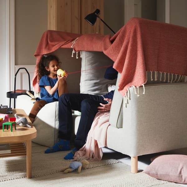 ベージュのPÄRUP/ペルプ ソファの上につくった毛布の秘密基地の中で女の子と男性が遊んでいる。そばに敷かれたベージュのラグの上にオーク材突き板のコーヒーテーブルが置かれている。