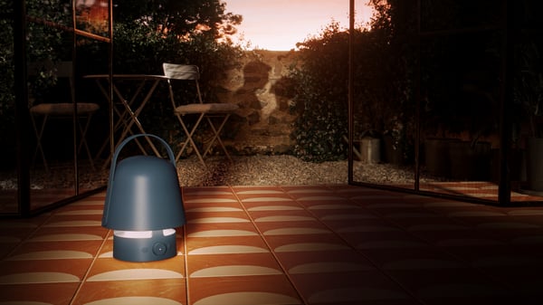 Blå lampa står på orange och vit mönstrad kakelgolv utomhus. Skuggorna av man och kvinna syns mot tegelvägg i bakgrunden