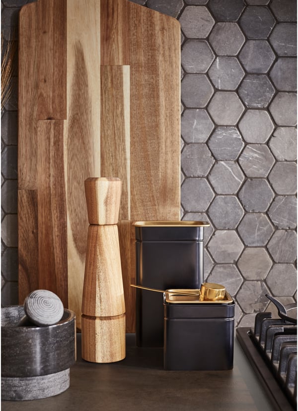 Black, brass, stone, metal and hearty wood textures in kitchen accessories, including a mortar and pestle, chopping board and pepper shaker.