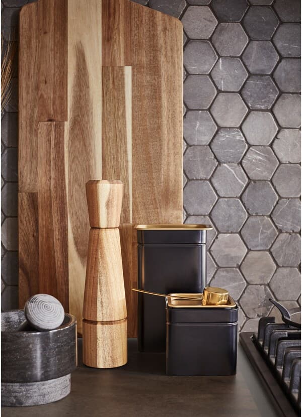 Black, brass, stone, metal and hearty wood textures in kitchen accessories, including a mortar and pestle, chopping board and pepper shaker.