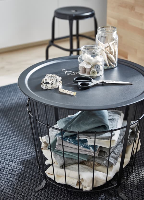 Black coffee table with wired basket bottom and removable tray tabletop, holding scissors and sewing supplies on top.