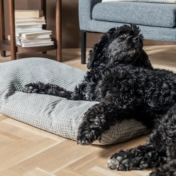 Black dog leaning on a grey LURVIG pet cushion.