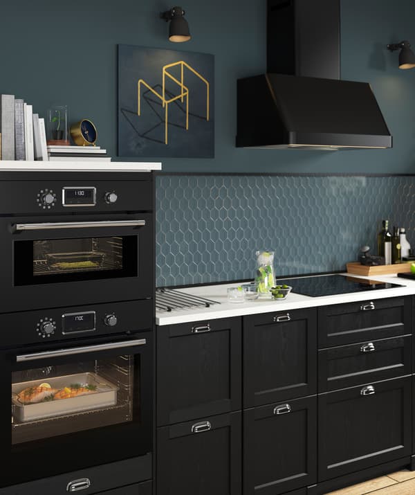 Black kitchen with blue walls, extractor hood and built-in ovens.