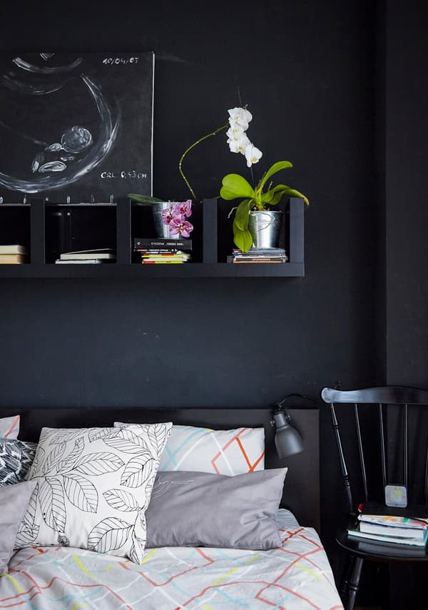 Black shelves above a bed, holding plants and books.