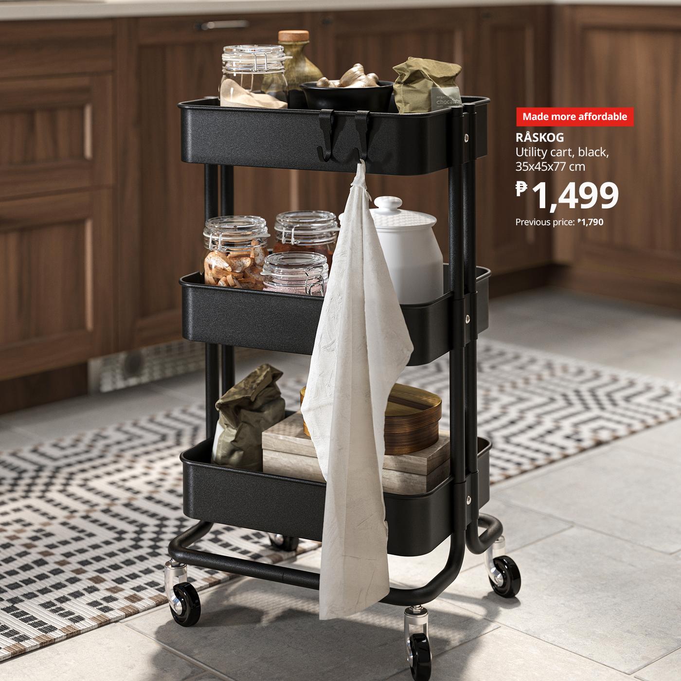 Black utility cart with three shelves holding jars and kitchen items, set in a cozy kitchen. A towel hangs on the side. Price tag: ₱1,499.