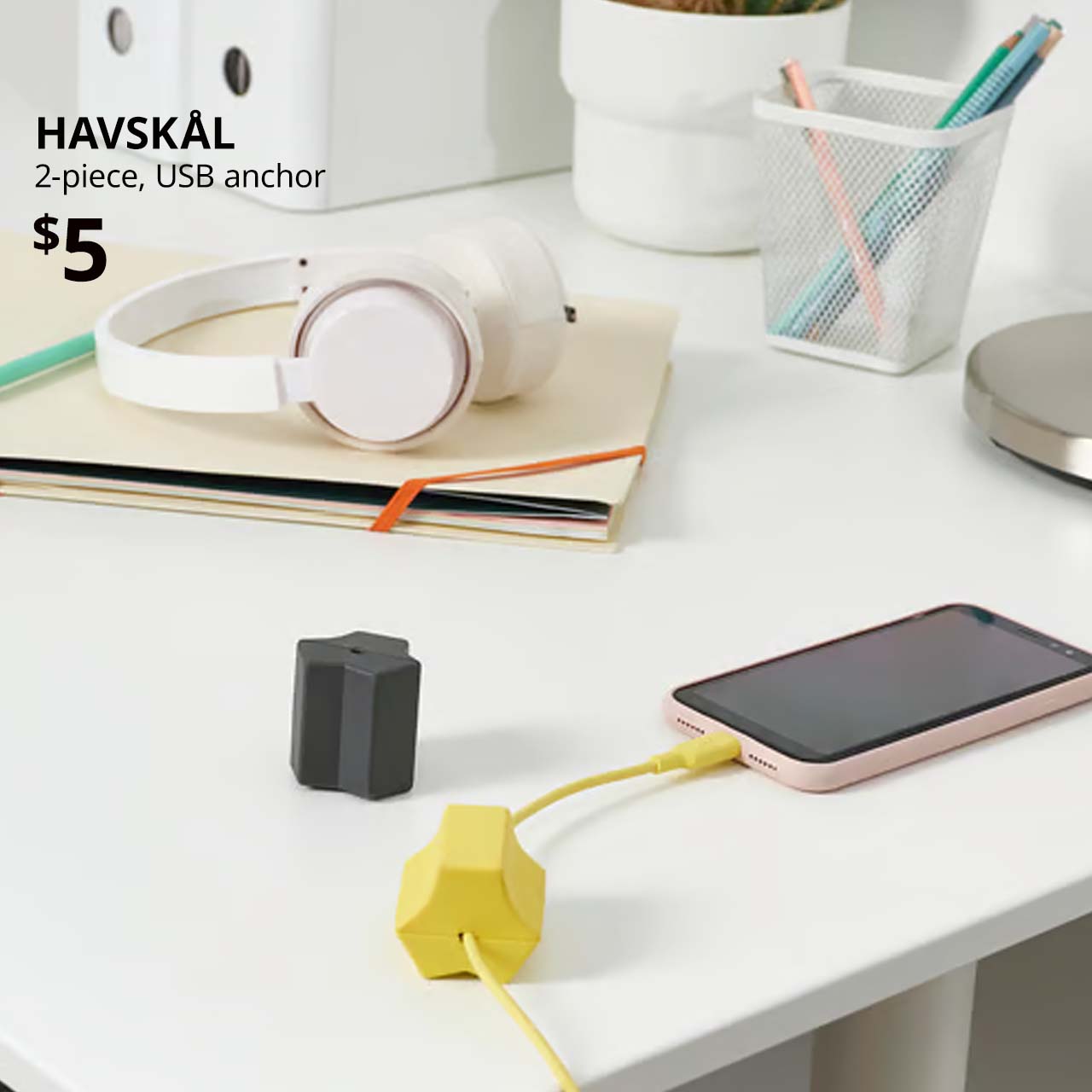 Black/yellow HAVSKÅL 2-piece, USB anchors, on home desk with cables running through the holders connected to a mobile phone.