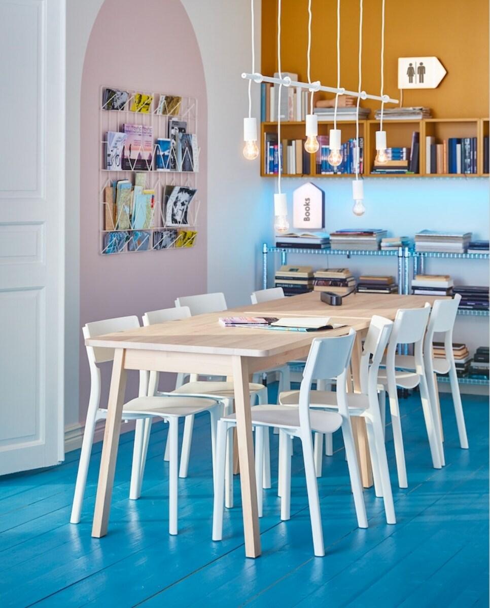 Blagovaonica s drvenim stolom i bijelim stolicama, plavi pod, police s knjigama i viseće žarulje.