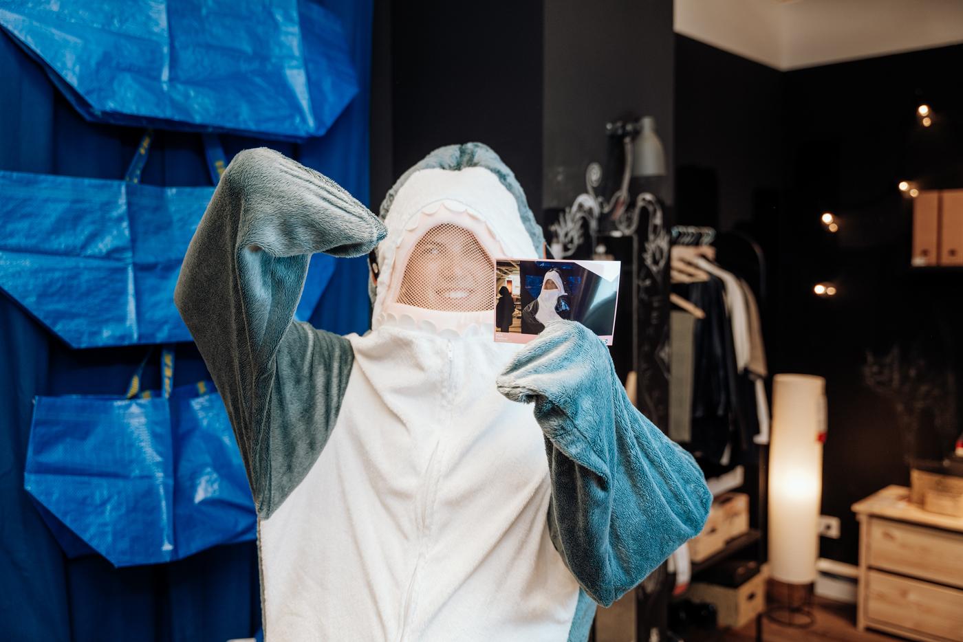 BLAHAJ posiert mit einem Foto in der Hand vor FRAKTA Taschen.