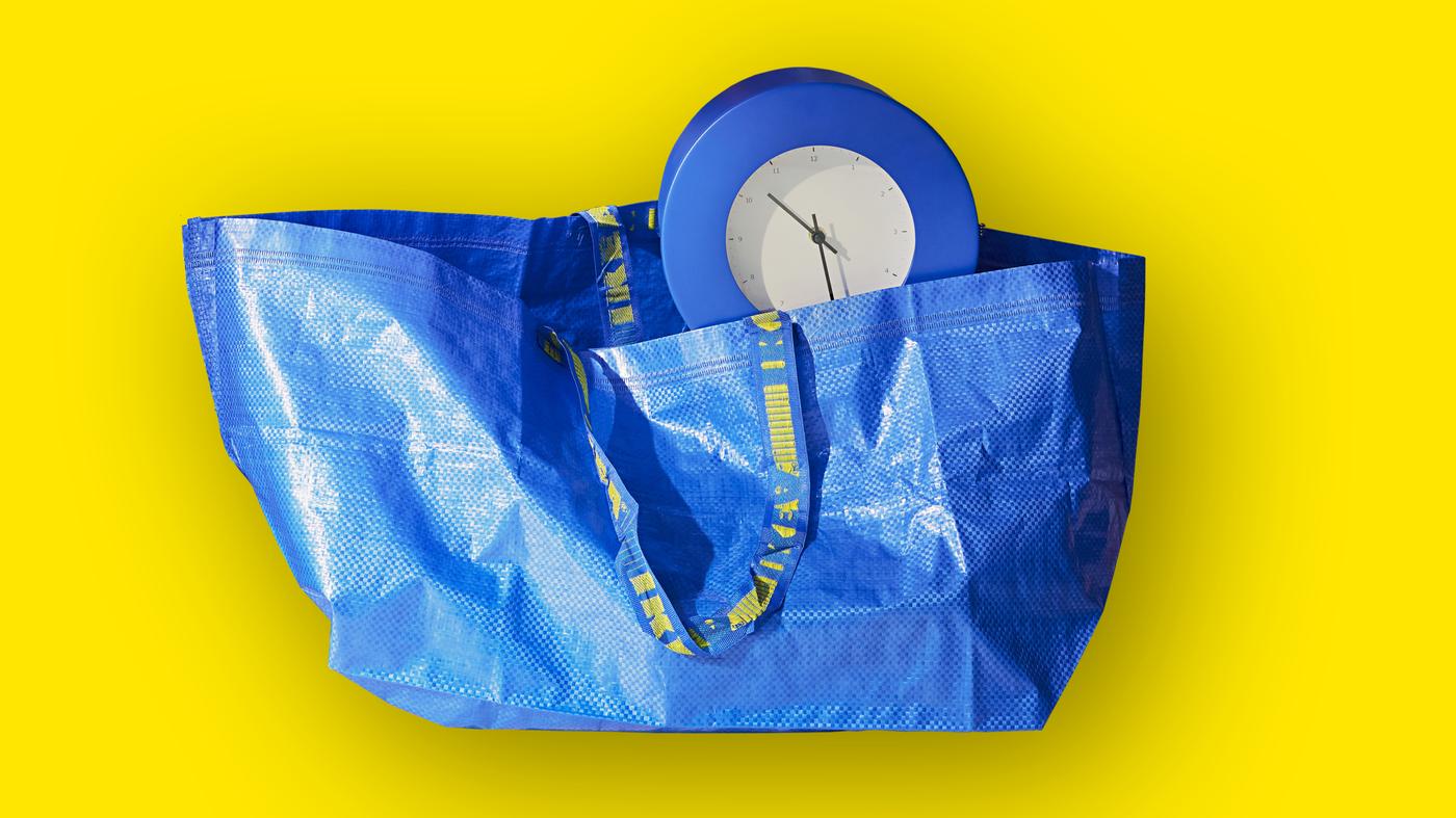 Blaue IKEA FRAKTA Tasche mit einer herausstehenden blauen Uhr auf gelbem Hintergrund.