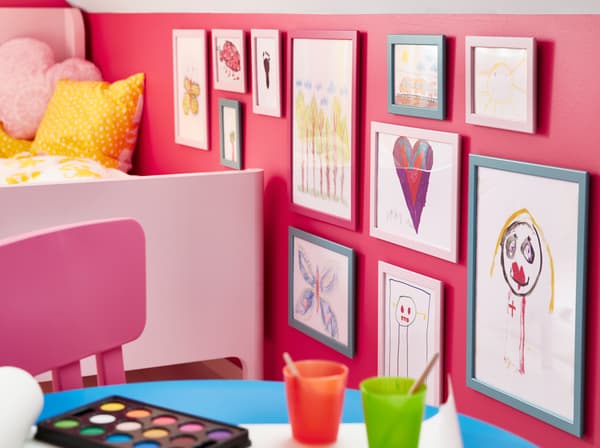 Blauwe en roze IKEA FISKBO lijsten in hardboard gebruikt om kindertekeningen in te lijsten.