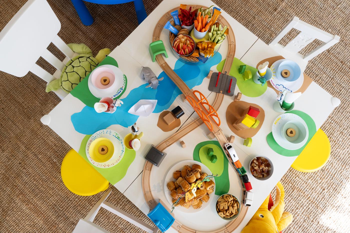 Blick auf den Geburtstagstisch. Eine LILLABO Eisenbahn fährt um die Snacks und gedeckten Teller herum. 