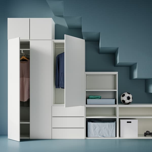Blick auf einen weißen PLATSA Kleiderschrank mit unterschiedlich hohen Elementen. Darin sind Kleidung, eine Tasche, Boxen, Gewichte und ein Fußball zu sehen.