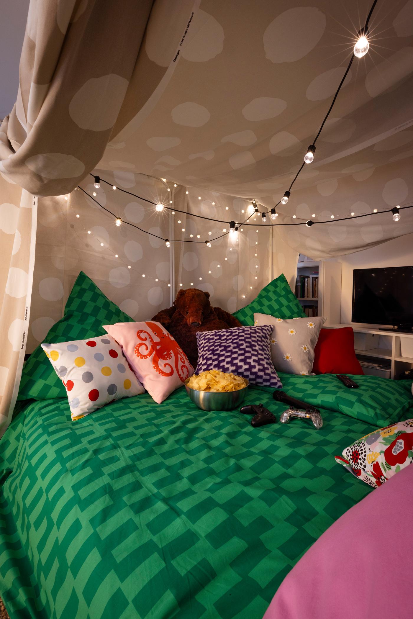 Blick in die Liegewiese. Man sieht schöne grüne Bettwäsche jede Menge Kissen und eine Lichterkette. 