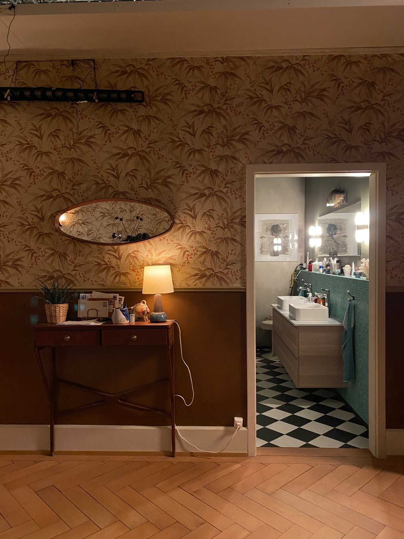 Blick vom Flur auf eine geöffnete Badezimmertür, hinter der man einen Waschtisch sieht.