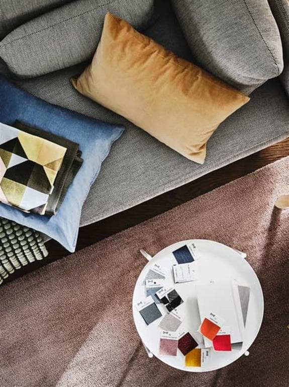 Blick von oben auf ein graues Sofa. Davor steht ein weißer runder Couchtisch mit Stoffmustern für Sofas.