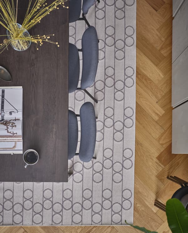 Blick von oben auf einen RINDSHOLM Teppich mit geometrischem Muster unter einem Ausziehtisch mit grauen Stühlen