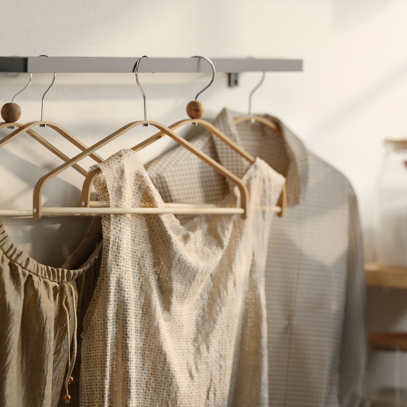 Blouses and shirts hanging on several HÖSVANS hangers in natural bamboo, hang on a metal wall-mounted rail.