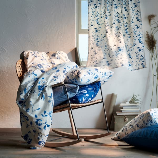 Blue and white floral textiles on a rattan rocking chair, and a floral curtain across a window behind.
